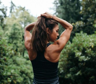 Frau schaut während des Workouts draußen über ihre Schulter Frau hält sich während des Workouts draußen die Haare zusammen und schaut schaut dabei über ihre Schulter